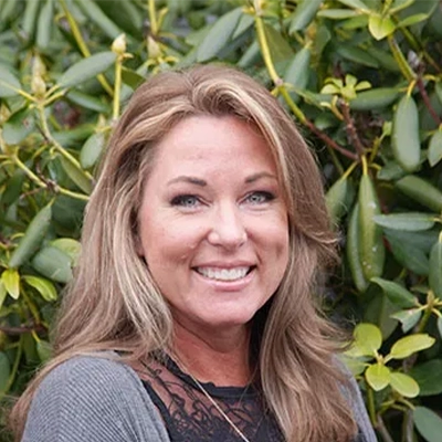 Hansen Dentistry Staff Member Kristine Smiling In Front Of Shrub