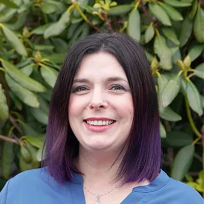 Hansen Dentistry Staff Member Stephanie Smiling In Front Of Shrub